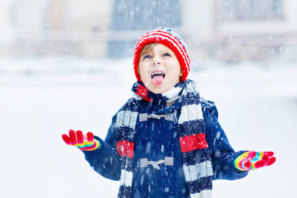 Preschool kid boy in colorful clothes playing outdoors during strong snowfall. Active leisure with children in winter on cold snowy days. Happy child having fun, playing with snow. Winter fashion