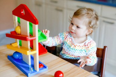 Küçük kız evde ya da çocuk odasında eğitici oyuncaklarla oynuyor. Mutlu sağlıklı çocuk renkli tahta top pisti ile eğleniyor. Çocuk top tutmayı ve yuvarlanmayı öğreniyor. Motorik eğitim