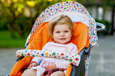 Bebek arabasında ya da bebek arabasında oturan ve yürüyüşe çıkan tatlı, gülümseyen bir kızın portresi. Mutlu şirin bebek dışarıda eğleniyor. Sağlıklı kız.