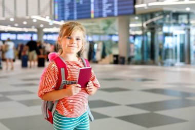Havaalanı terminalindeki küçük anaokulu kızı. Mutlu çocuk uçakla tatile çıkıyor. Pasaportu ve çantası olan gülümseyen çocuk.
