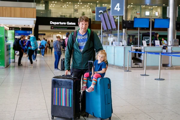 Cute little toddler girl and father at the airport. Happy family traveling by plane, making vacations. Young dad and baby daughter with suitcases waiting for flight. Family going on journey. Ireland.