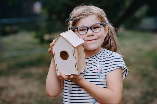 可爱的笑容可亲的金发姑娘站在新手工制作的嵌套箱边 抱着木制鸟舍的学龄前儿童 — 图库照片