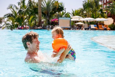 Şirin mutlu küçük yürümeye başlayan çocuk kız ve babası havuzu ve sahip eğlenceli bir otel resort aile tatil üzerinde. Sağlıklı çocuk ve suda oynayan adam. Bebek kızı renkli moda mayo