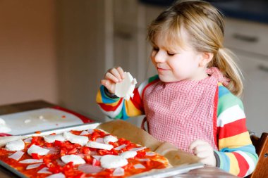 Sevimli küçük kız evde İtalyan pizzası yapıyor. Ev mutfağında, evde eğlenen sevimli mutlu çocuk. Çocuk, anaokulu öğrencisi sağlıklı yemek hazırlıyor ve yardım ediyor..