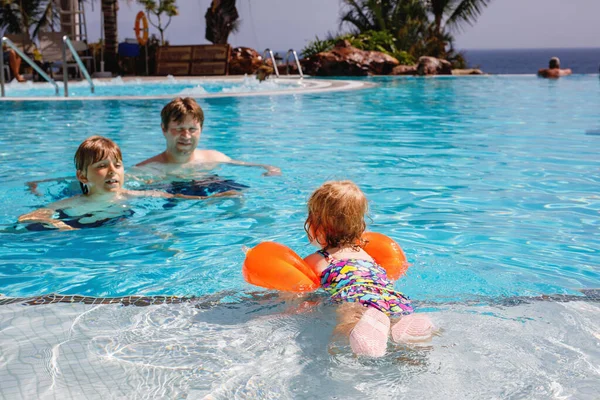 Cute happy little toddler girl, school kid boy and father in the pool and having fun on family vacations in a hotel resort. Healthy children and man playing in water.