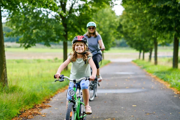 Happy family is riding bikes outdoors and smiling. Mother and daughter, cute little preeschool girl on bicycles, active leisure and sports together