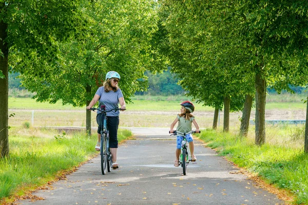 Happy family is riding bikes outdoors and smiling. Mother and daughter, cute little preeschool girl on bicycles, active leisure and sports together