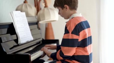 Okullu çocuk oturma odasında piyano çalıyor. Çocuk müzik aleti çalmayı öğrenirken eğleniyor. Yetenekli genç kız içeride..