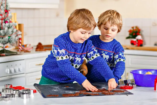 Two little preschool boys baking gingerbread cookies. Happy siblings, children in xmas sweaters. Kitchen decorated for Christmas. Brothers fighting, making trouble chaos. Christmas family activity.