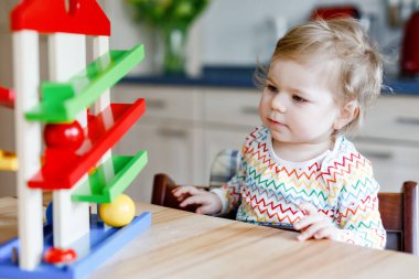 Küçük kız evde ya da çocuk odasında eğitici oyuncaklarla oynuyor. Mutlu sağlıklı çocuk renkli tahta top pisti ile eğleniyor. Çocuk top tutmayı ve yuvarlanmayı öğreniyor. Motorik eğitim