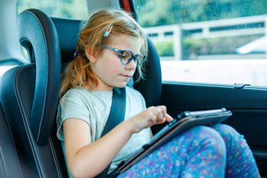 Küçük kız arabanın içinde tablet oynuyor. Aile tatile çıkıyor. Anaokulu çocuğu eğleniyor