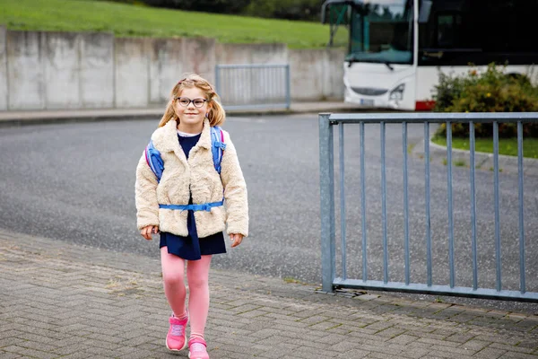 小学校の子供たち 屋外の建物の近くにバックパックを持っている小さな女の子 レッスンスタート 秋の初日でした バスで通学する子供 — ストック写真