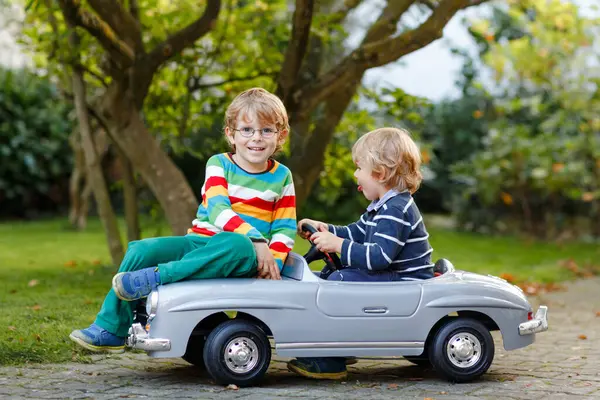 两个学龄前的小男孩在夏天的花园里玩着一辆大的旧玩具车 在户外 快乐的孩子们一起玩 孩子们的户外活动 温暖的日子里的兄弟姐妹和朋友 — 图库照片