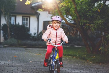 Küçük anaokulu kızı bisiklete biniyor. Bisikletli çocuk dışarıda. Sıcak bir yaz günü okula giderken bisiklet sürmekten hoşlanan mutlu bir çocuk. Anaokulu öğrencisi kaskla bisiklete binmeyi öğreniyor.