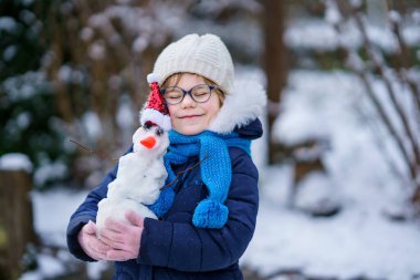 Cute little preschool girl with glasses making mini snowman. Adorable healthy happy child playing and having fun with snow, outdoors on cold day. Active leisure with children in winter.