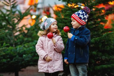İki küçük çocuk, evlat gülümseyerek ve yeme kız Alman noeli pazarında şekerli elma crystalized. Arka plan ışığı elbiseyle kış mutlu arkadaş. Aile, geleneği, tatil kavramı.