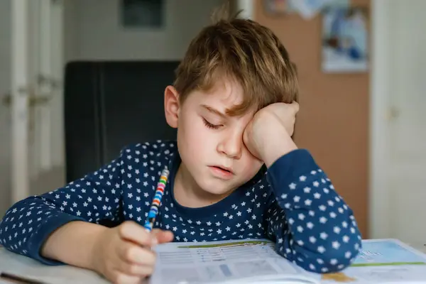 Hard-working sad school kid boy making homework. Upset tired child on home schooling, learning