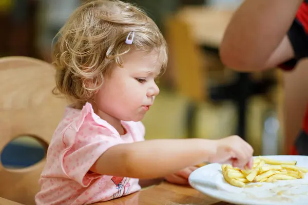 愛らしい幼児の女の子が健康野菜と不健全なフレンチ フライ ポテトを食べるします 保育園や保育園の食堂で皿から食べ物を取ってかわいいハッピー ベビー子供 — ストック写真