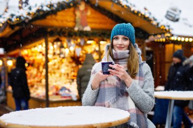 Güzel genç bir kadın sıcak punç içiyor, Alman Noel pazarında sıcak şarap içiyor. Kış kıyafetleri içinde mutlu bir kız. Arka planda ışıklar var. Berlin, Almanya 'da kış günü kar tatilinde.
