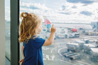 Havaalanında küçük tatlı bir kız, seyahat ediyor. Pencerenin yanında bekleyen ve uçakları izleyen mutlu sağlıklı çocuk. Aile uçakla yaz tatiline çıkıyor.