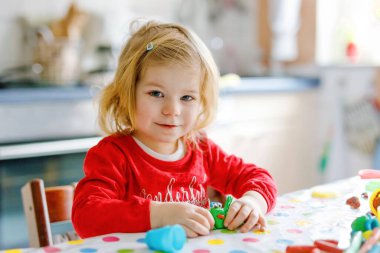 Renkli killi, sevimli, küçük bir kız. Sağlıklı bebek oyun oynuyor ve oyun hamurundan oyuncaklar yapıyor. Küçük çocuk kil kalıp ve öğrenim.