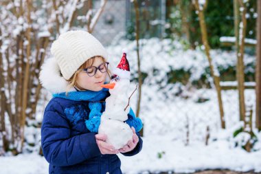 Cute little preschool girl with glasses making mini snowman. Adorable healthy happy child playing and having fun with snow, outdoors on cold day. Active leisure with children in winter.