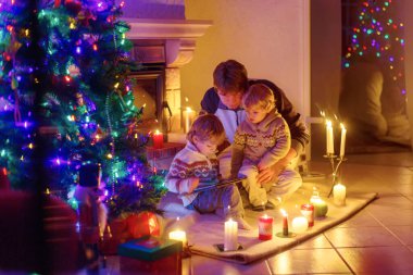 Baba ve Noel arifesi zamanında şömine baca tarafından oturan iki küçük çocuğu. Baba ve çocuklar çocuklar oğulları tablet ile oynuyor. Açık havada kar yağışı sırasında gelen pencereden. Aile xmas kutluyor