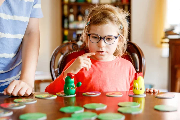 Family playing board game at home. Kids play strategic game. Little sister girl moving part of table game. Fun indoor activity. Siblings bond. Educational toys