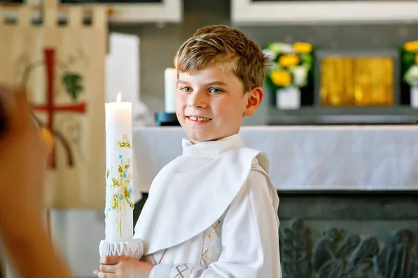 stock image Little kid boy receiving his first holy communion. Happy child holding Christening candle. Tradition in catholic curch. Kid in a white traditional gown in a church near altar