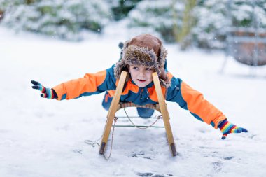 Küçük çocuk kar yağışı sırasında kızak sürmekten hoşlanıyor. Eski model kızakla gezen mutlu anaokulu çocuğu. Çocuk dışarıda karla oynuyor. Kışın aile Noel tatili için aktif eğlence.