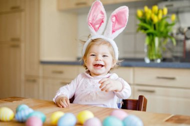 Paskalya tavşanı kulakları takan tatlı küçük kız renkli pastel yumurtalarla oynuyor. Mutlu bebek hediyeleri açıyor. Pembe elbiseli sevimli, sağlıklı çocuk aile tatilinin tadını çıkarıyor.,