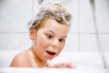 Şampuan köpüğü ve banyo yapan saçlarında kabarcıklar olan tatlı bir çocuk. Gülümseyen anaokulu kızı sağlık hizmetleri ve hijyen konseptinin portresi. Saçlarını kendi yıkar.