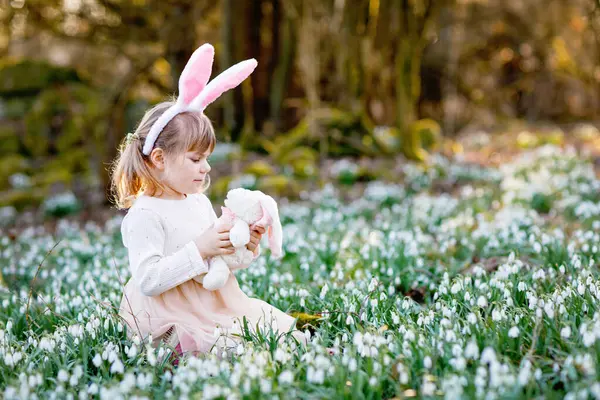 晴れた日に春の森の中で柔らかいぬいぐるみを保持イースターバニーの耳を持つ愛らしい女の子 雪の花がたくさんあるかわいい幸せな子供 キリスト教の休日の概念 — ストック写真