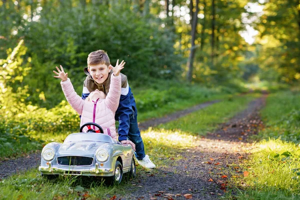 两个快乐的孩子在秋天的森林里玩着又大又旧的玩具车 男孩儿和小女孩一起开车和开车 里面有可爱的妹妹 笑着笑着的孩子 可爱的家庭 — 图库照片