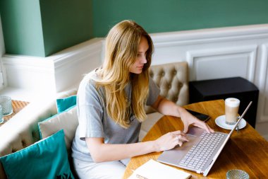 Akıllı telefon teknolojisi kullanan ve dizüstü bilgisayara bakan genç bir kadının portresi. Restoranda ya da kapalı kafede kahveli dizüstü bilgisayar kullanan genç bir kadın. Merkez ofis kavramı
