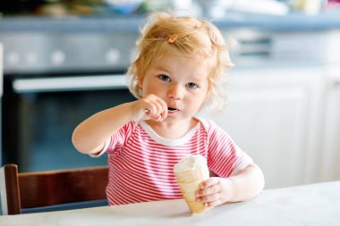 Tatlı bebek waffle külahında kaşıkla tatlı dondurma yiyor. Yemek, çocuk, beslenme ve gelişim konsepti. Sevimli bebek, kaşıklı kız sandalyede oturuyor ve kendi kendine yemek yiyor..