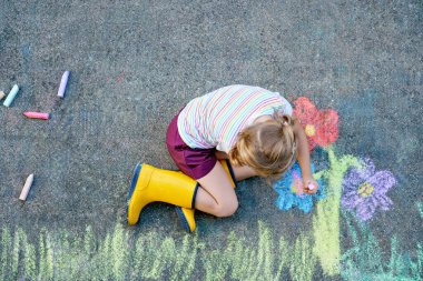 Sevimli küçük kız ve asfalta renkli tebeşirle boyanmış çiçekler. Mutlu anaokulu çocuğu tebeşirle resim yaparken eğleniyor. Çocuklar için yaratıcı eğlence, çizim ve resim