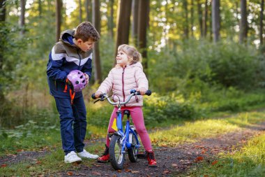 Erkek kardeş, kız kardeş, kız kardeş bisiklet kaskını kafasına taktı. Kardeş mutlu çocuk bisikleti öğretiyor ve bisikletle eğleniyor. Aktif aile fertleri açık havada. Çocuk aktivitesi.