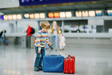 Bavullu şirin bir çocuk, uluslararası havaalanında iki bavulu var. Anne ve küçük kızı arka planda, mutlu bir aile uçuşa hazırlanıyor ve tatile çıkıyor. Seyahat yaşam tarzı