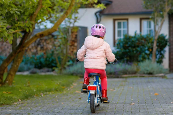 Little preschool girl riding bike. Kid on bicycle outdoors. Happy child enjoying bike ride on her way to school on warm summer day. Preschooler learning to balance on bicycle in safe helmet