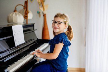 Müzik okulunda piyano çalan güzel bir anaokulu kızı. Sevimli çocuk müzik aleti çalmayı öğrenirken eğleniyor. Çocuklar için erken müzik eğitimi.
