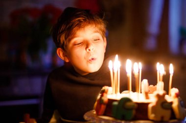 Sevimli, mutlu, küçük sarışın çocuk doğum gününü kutluyor. Çocuk ev yapımı kek üzerine mum üflüyor, kapalı alanda. Okul çocukları için doğum günü partisi, aile kutlaması.