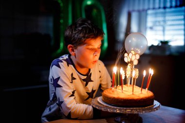 Sevimli, mutlu, küçük sarışın çocuk doğum gününü kutluyor. Çocuk ev yapımı kek üzerine mum üflüyor, kapalı alanda. Okul çocukları için doğum günü partisi, aile kutlaması.