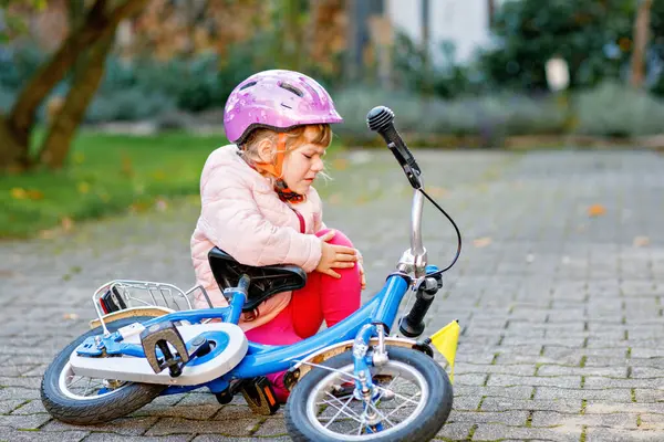 彼女の自転車から落ちた後 地面に座っているかわいい少女 自転車に乗っている間 安全なヘルメットで子供を泣かせて 怪我をする 子供とアクティブな家族のレジャー — ストック写真