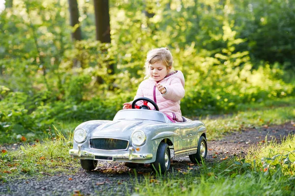 ビンテージのおもちゃの車を運転する小さな幼稚園の少女 アウトドアで遊ぶのが楽しい子供たち 森で暖かい秋の日を楽しんでいるアクティブな幼稚園児 見事な — ストック写真