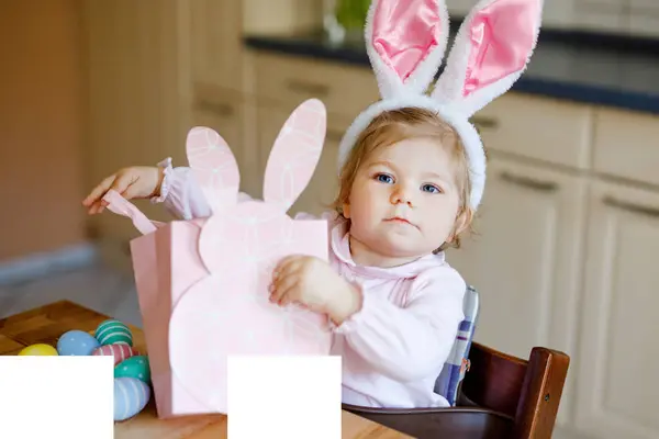かわいい小さな幼児の女の子は 色のパステルの卵で遊んでイースターバニーの耳を着ています 幸せな赤ちゃんの贈り物をアンパック ピンクの服で快適な健康的な笑顔の子供は家族の休日を楽しむ — ストック写真