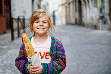 Şehrin sokaklarında taze Fransız ekmeğiyle sevimli, küçük bir anaokulu kızı. Paris, Fransa 'da küçük mutlu bir çocuk
