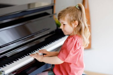 Oturma odasında piyano çalan güzel küçük kız. Sevimli anaokulu çocuğu müzik enstrümanı çalmayı öğrenirken eğleniyor. Çocuklar için erken müzik eğitimi