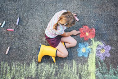 Sevimli küçük kız ve asfalta renkli tebeşirle boyanmış çiçekler. Mutlu anaokulu çocuğu tebeşirle resim yaparken eğleniyor. Çocuklar için yaratıcı eğlence, çizim ve resim