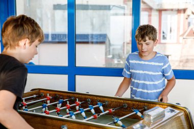 İki gülümseyen okul çocuğu masa futbolu oynuyor. Mutlu çocuklar aileleriyle ve arkadaşlarıyla oynayıp eğleniyorlar. Olumlu reşit olmayan çocuklar ya da gençler.